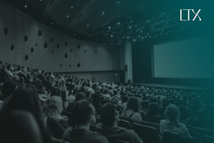 An audience in a darkened auditorium faces a glowing presentation screen, with the LTX logo at the top right.