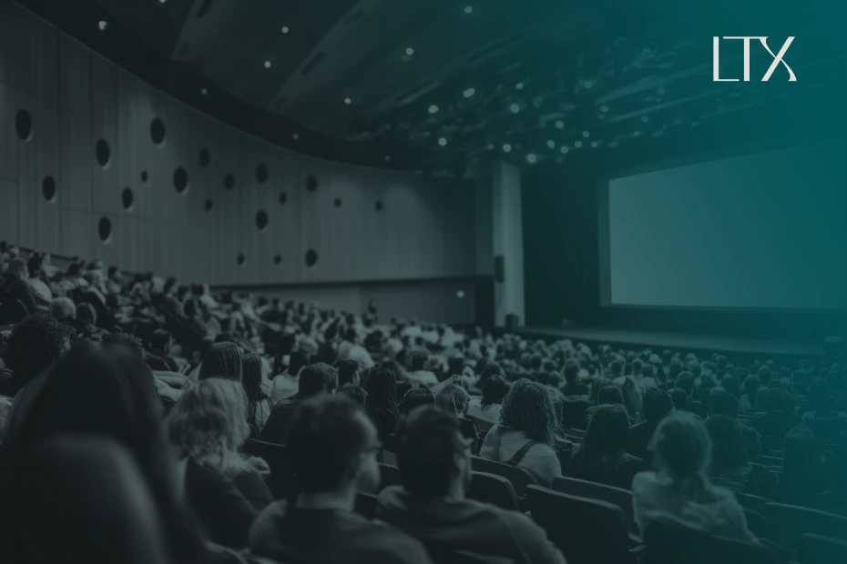 An audience in a darkened auditorium faces a glowing presentation screen, with the LTX logo at the top right.