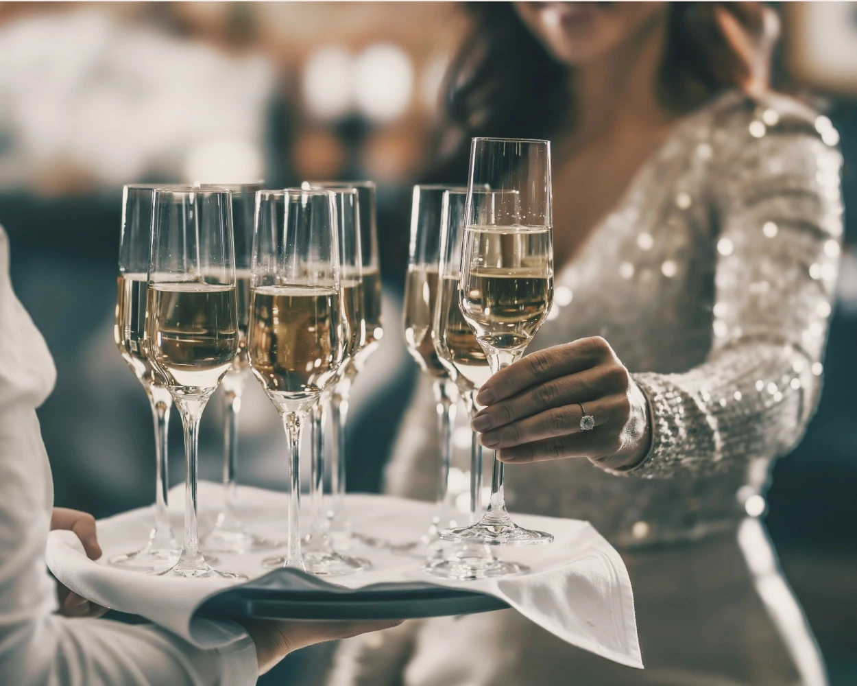 A guest in a sequinned dress takes a glass of Champagne from a server’s tray.